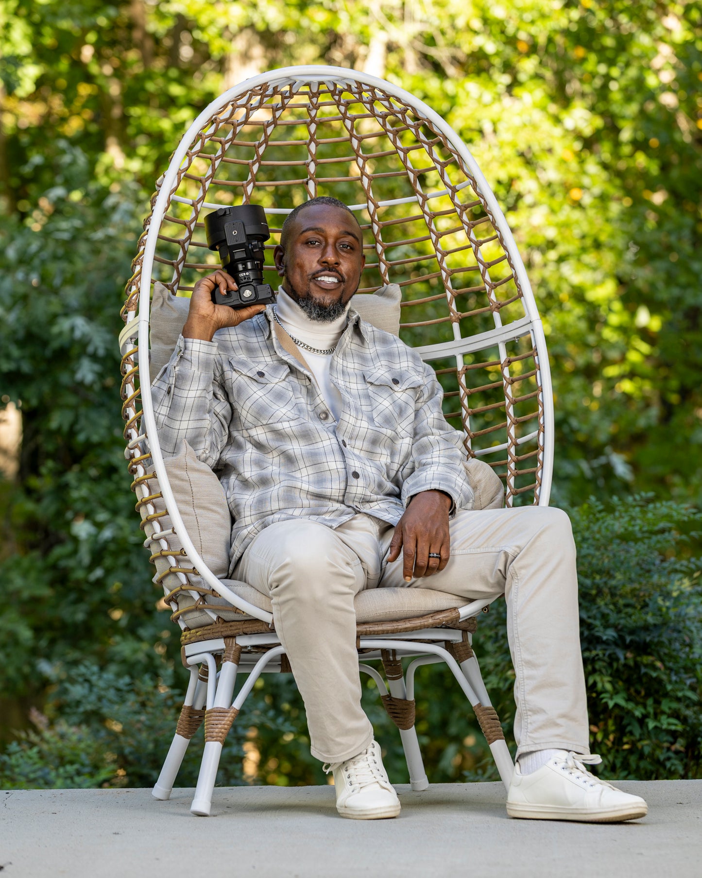 Man sitting in a wicker chair outdoors holding a camera | Shot By Lo