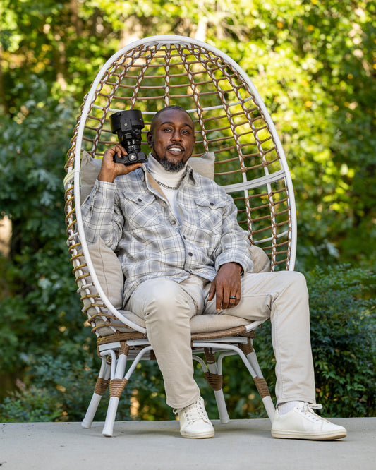 Man sitting in a wicker chair outdoors holding a camera | Shot By Lo